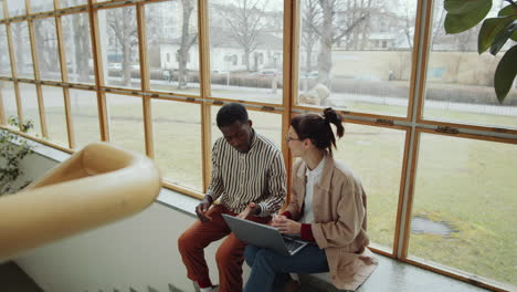 Man-and-Woman-Discussing-Project-on-Laptop-on-Window-Sill